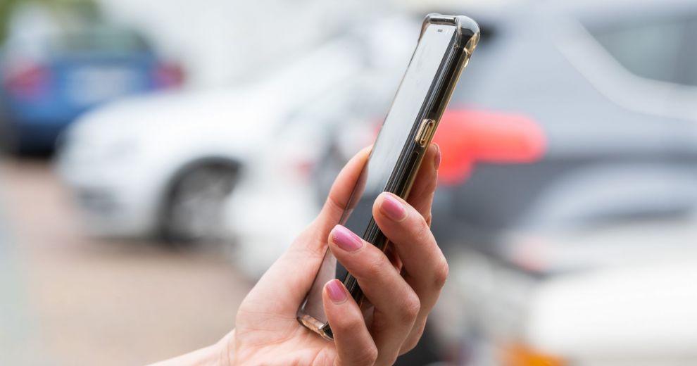 Eine Frau hält ein Handy, im Hintergrund parkende Autos