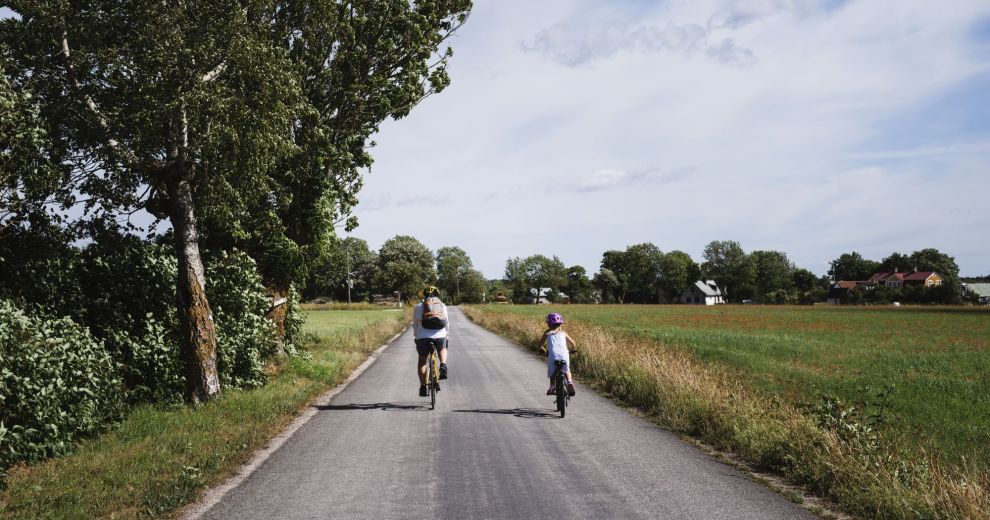 Vater und Tochter fahren mit dem Fahrrad auf einem Fahrradweg zwischen den Feldern einer Siedlung.