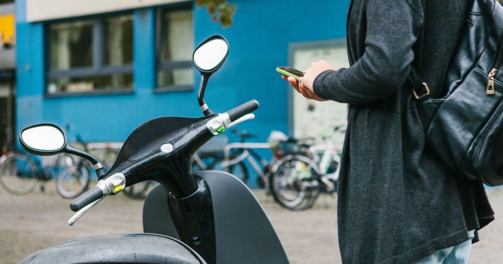 Ein Tourist mit einem Rucksack wird einen Elektro-Roller durch eine mobile Anwendung auf dem Telefon verwenden.