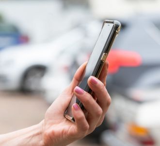 Eine Frau hält ein Handy, im Hintergrund parkende Autos