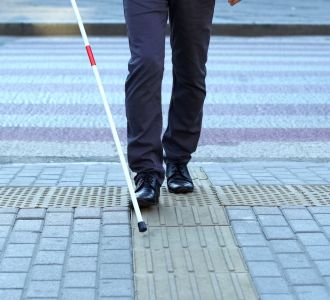 Sehbehinderte Person mit Blindenstock auf taktilen Fliesen.