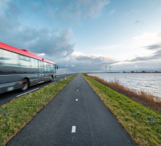 Schnellfahrender Bus entlang am See/Meer in ländlicher Landschaft.
