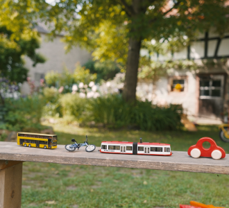 Spielzeugfiguren eines Busses, eines Fahrrads, eines Autos und eines Zuges auf einem Holztisch